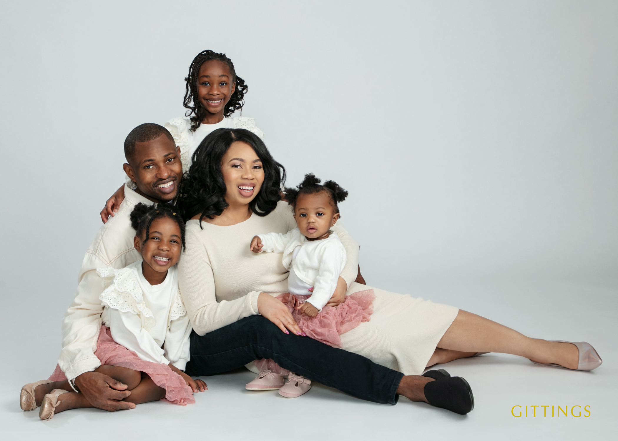 Family Portrait Of Parents And Three Young Children Wearing Coordinated Cream And Blush Outfits In A Studio Setting.