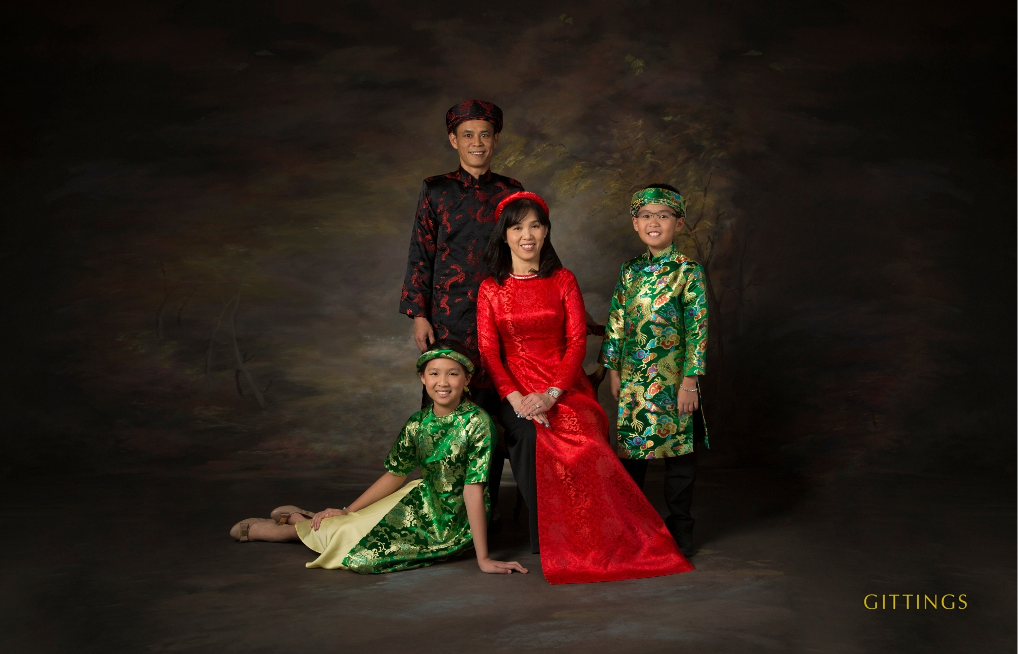 Studio Family Portrait Of Parents And Two Children Wearing Traditional Vietnamese Áo Dài In Vibrant Red, Green, And Black.